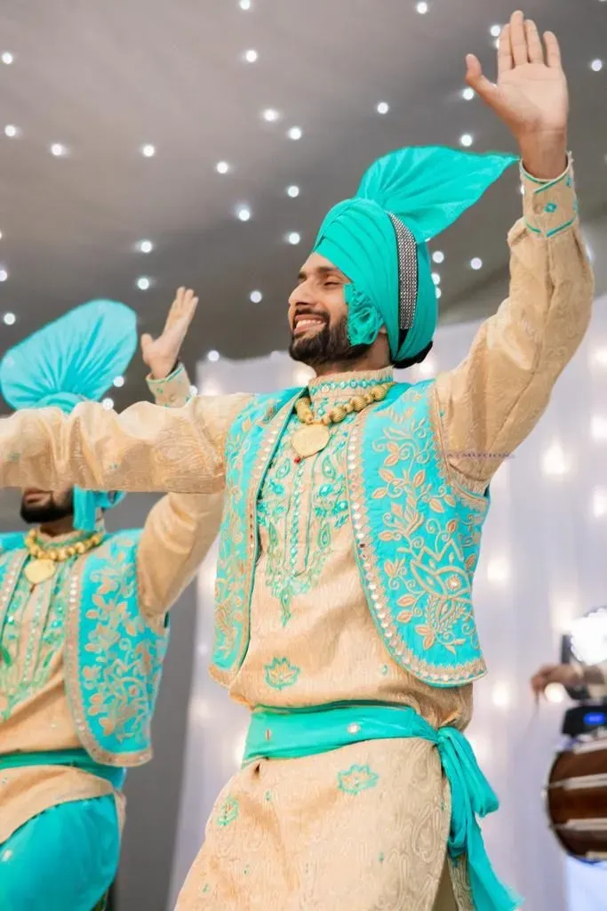 Bhangra dancer in teal and gold performing at a wedding reception