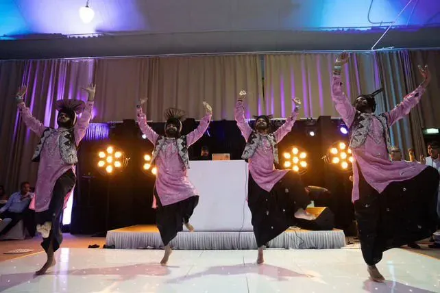 Bhangra dancers mid-jump in front of a DJ booth with lights