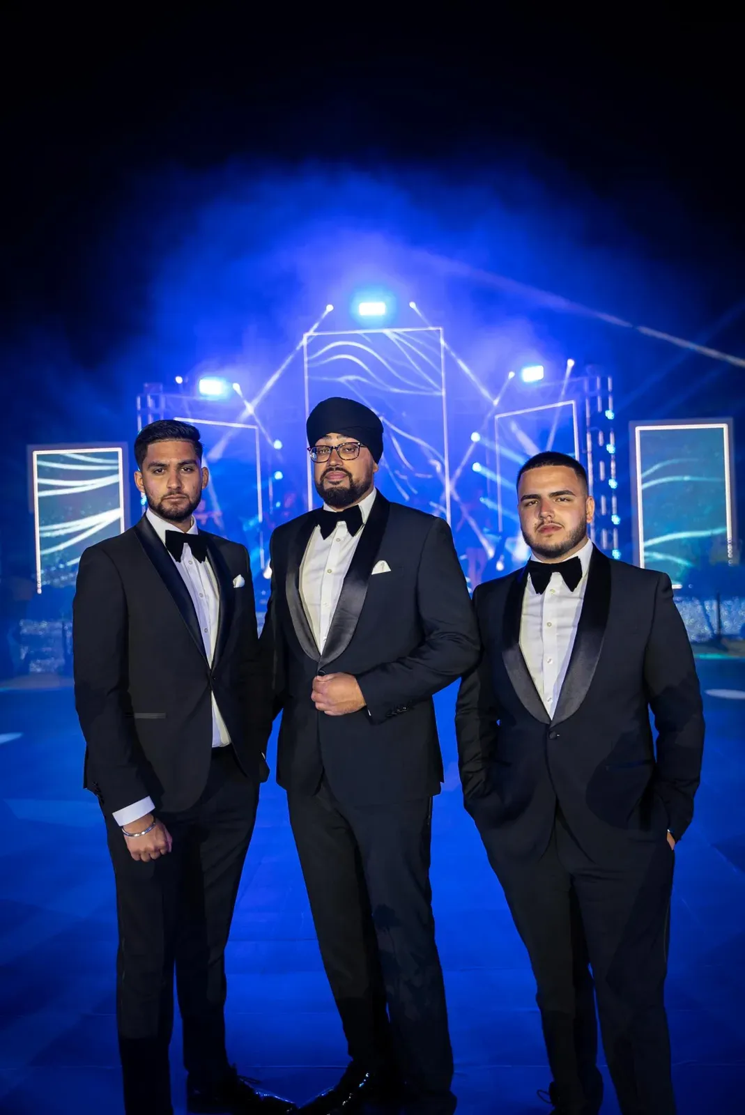 Three dhol performers in black tie on a lit stage