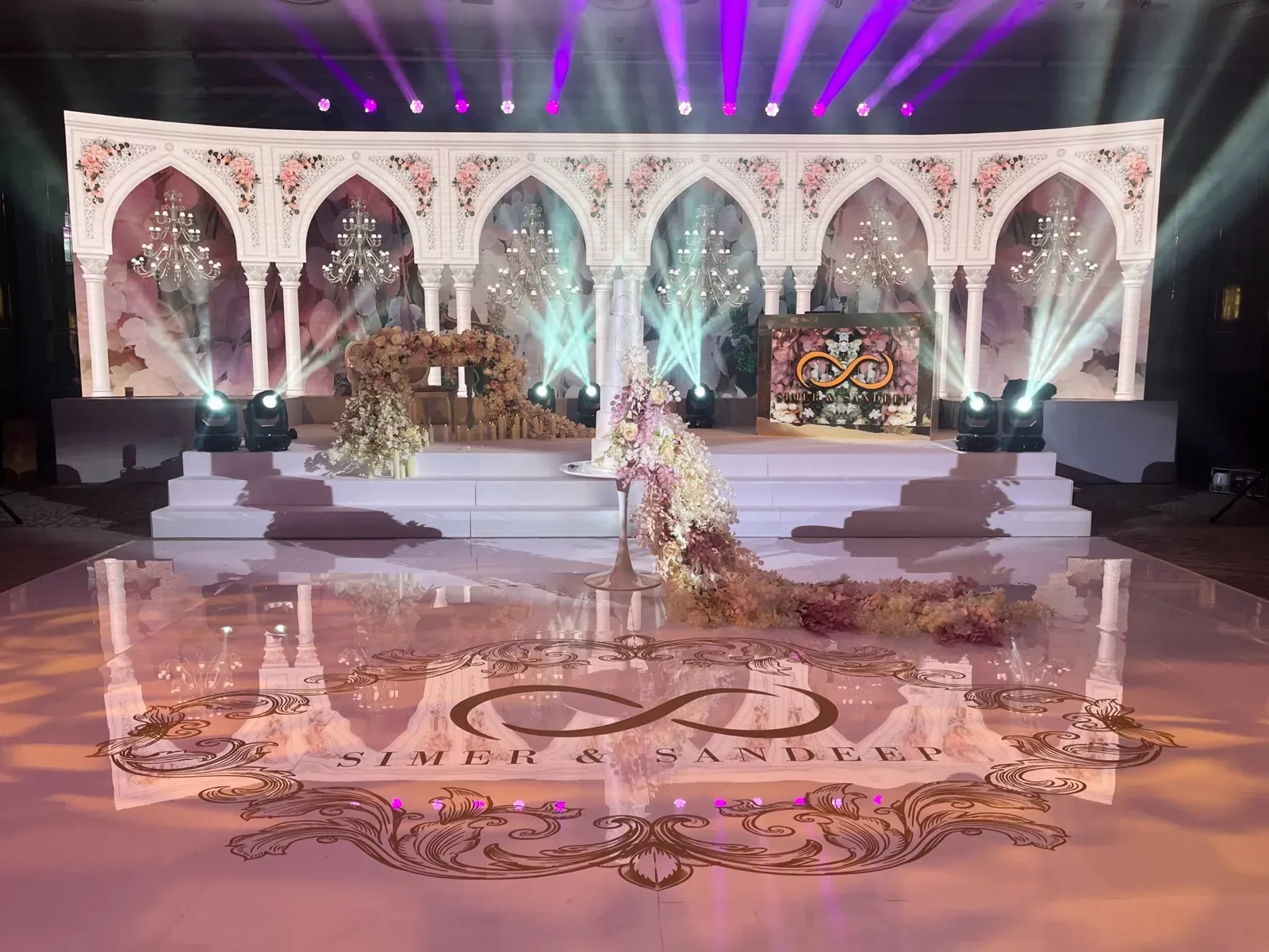 White arched stage set with moving lights and a printed monogram dance floor