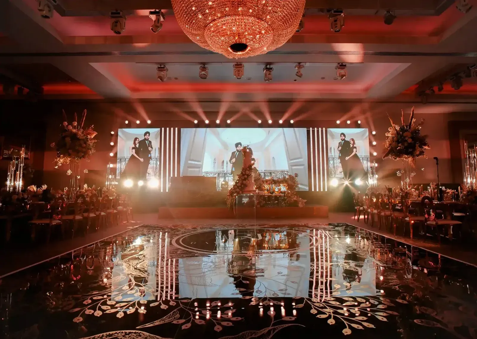 Mirror-effect dance floor reflecting an LED screen wall and stage at a wedding reception