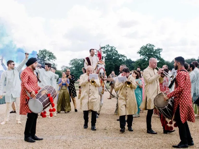 Band baja and dhol in red leading a baraat with the groom