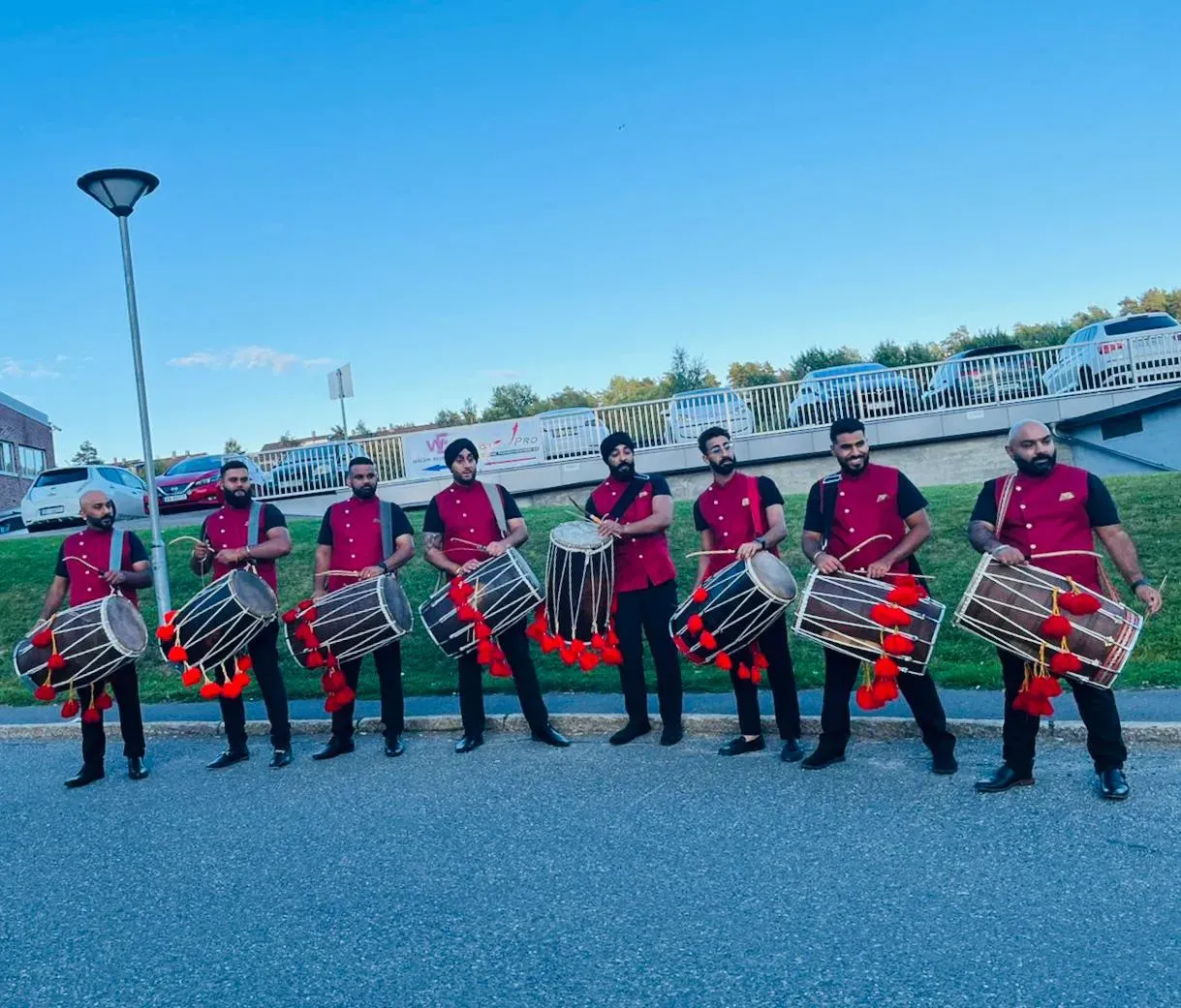 Band baja and dhol team in red sherwanis lined up outside a venue