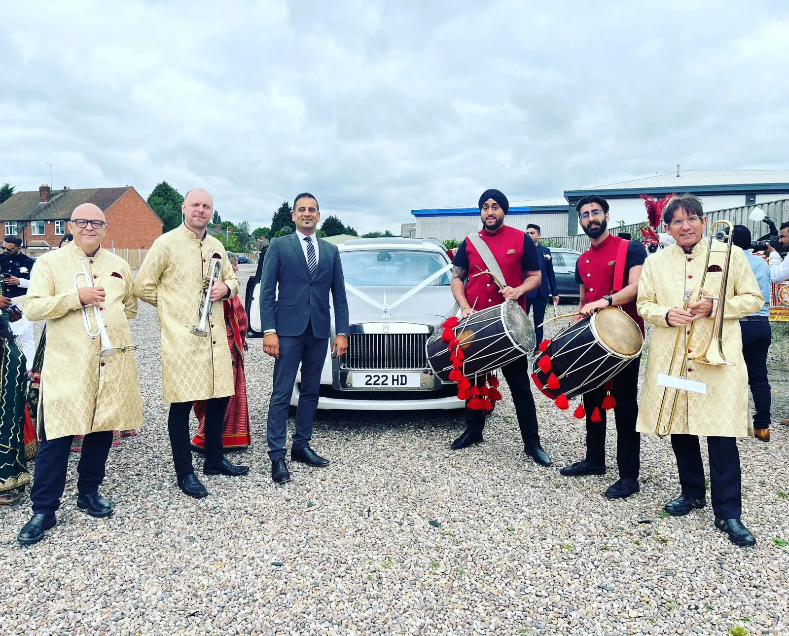 Band baja in red with the groom and family beside a wedding car