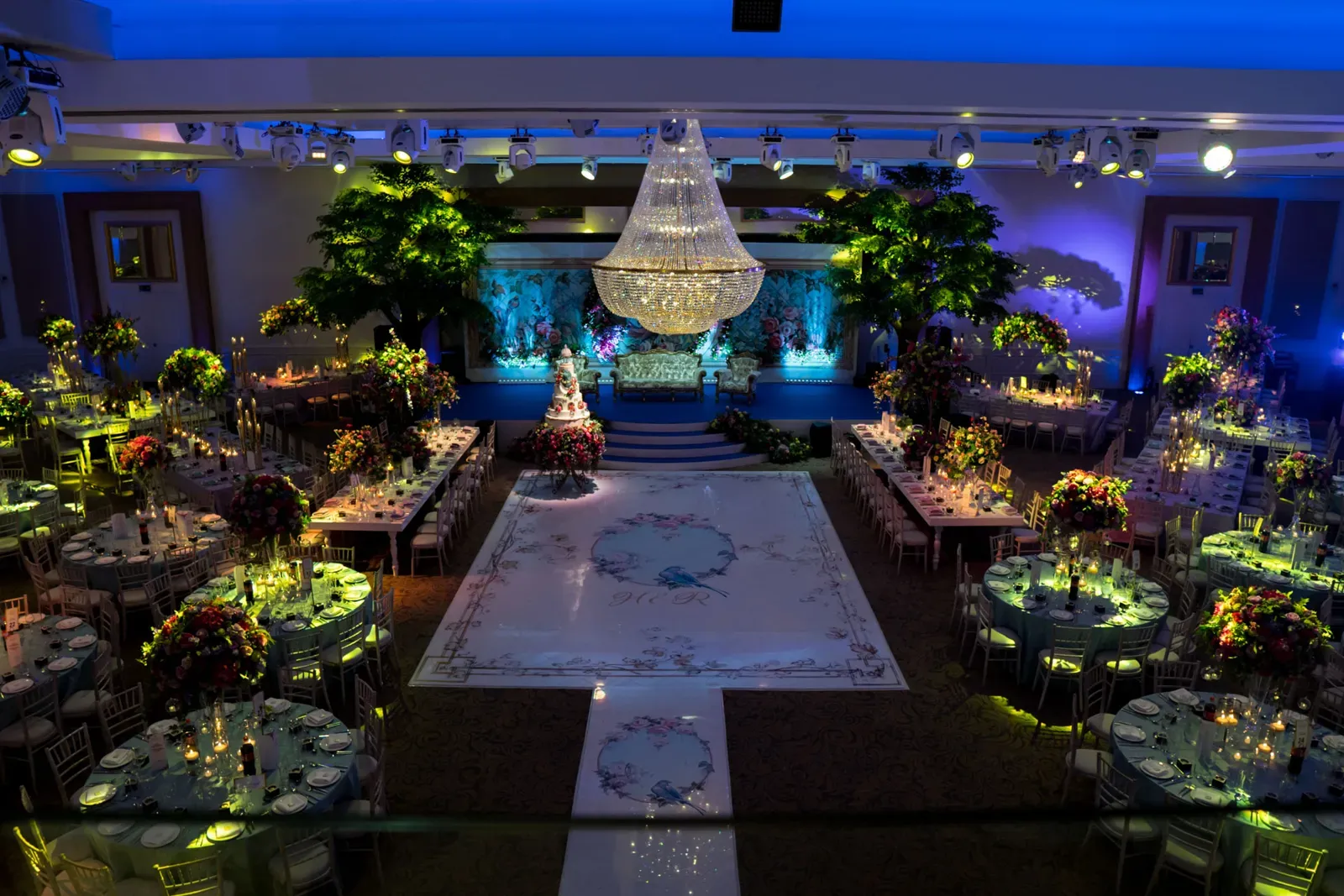 Ballroom styled as an enchanted garden with trees, chandelier and a white aisle