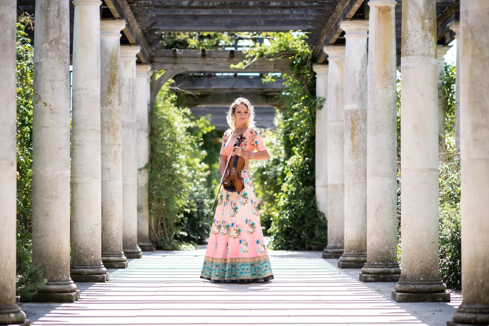 Violinist in a lehenga in a pillared garden walkway