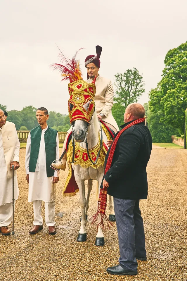 Groom seated on a decorated white horse with family beside him