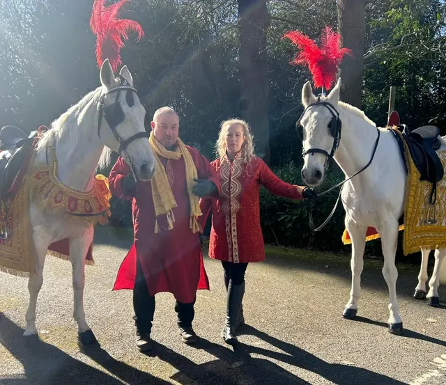 Two white wedding horses with handlers in traditional dress