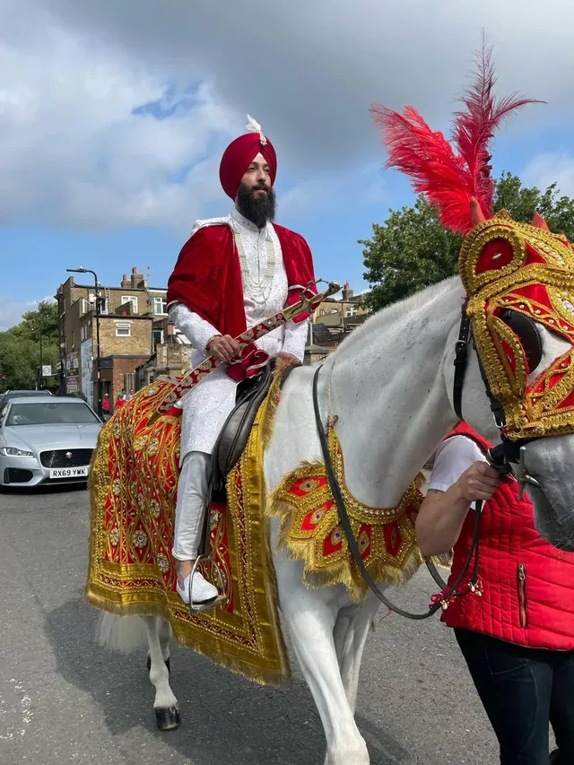 Sikh groom in red and gold riding a decorated white horse